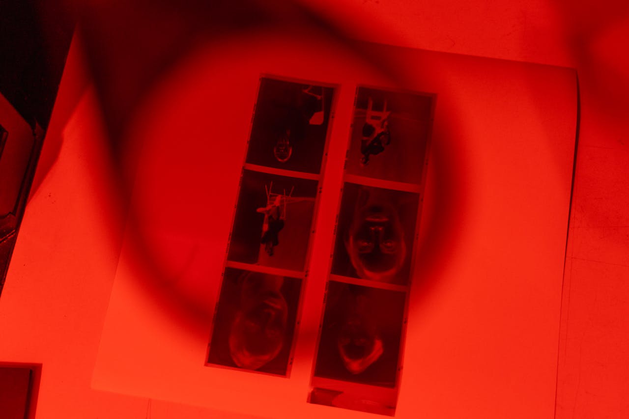 An atmospheric red photo lab showcasing filmstrip negatives under a magnifying lens.